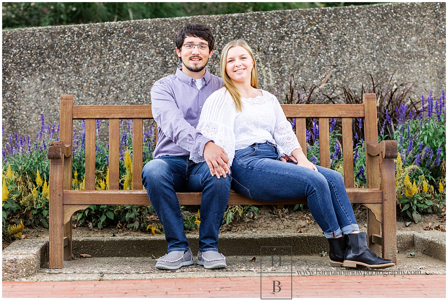 Couple sitting on bench in front of purple flower bed.