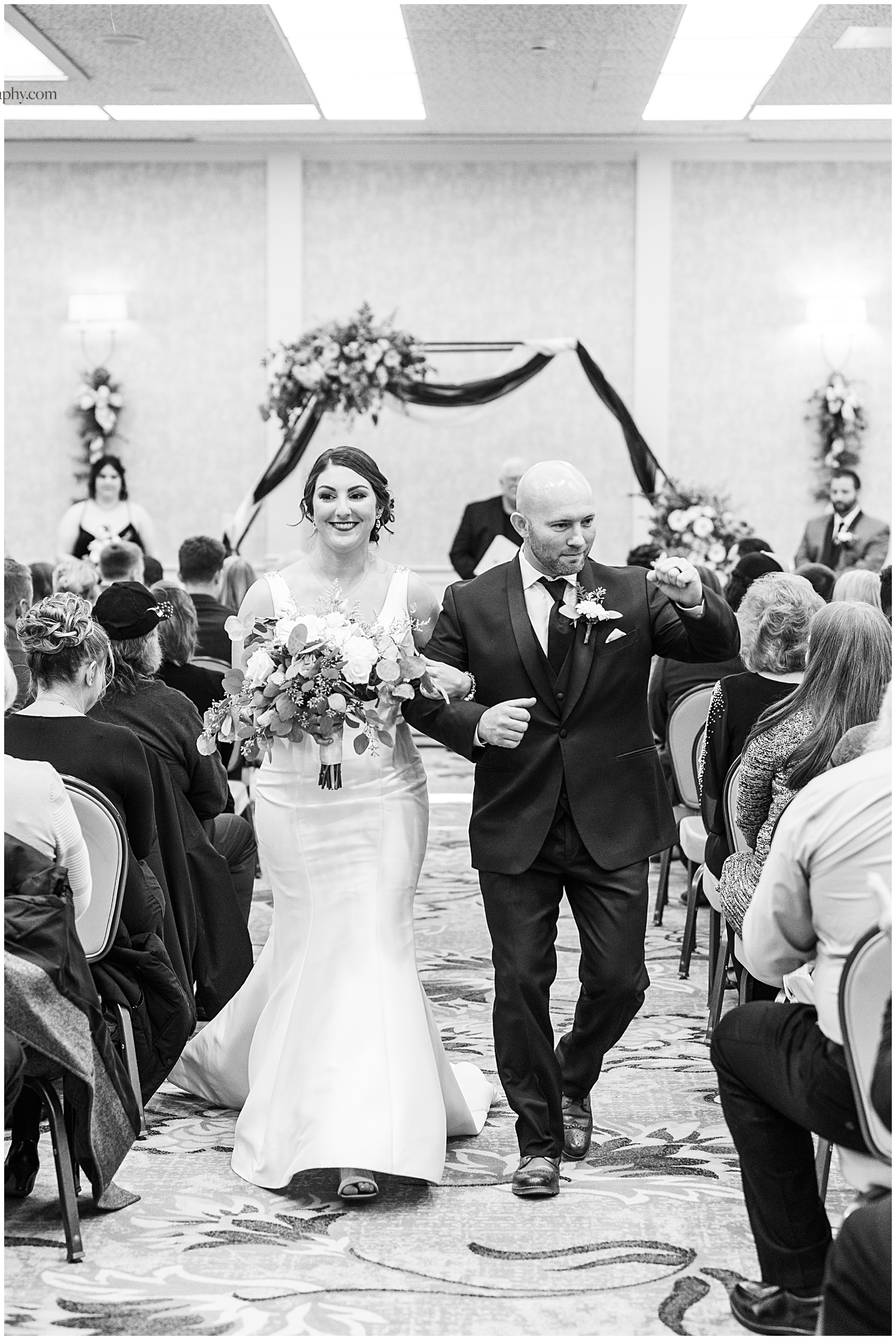 Black and white photo of couple walking down the aisle after wedding ceremony.