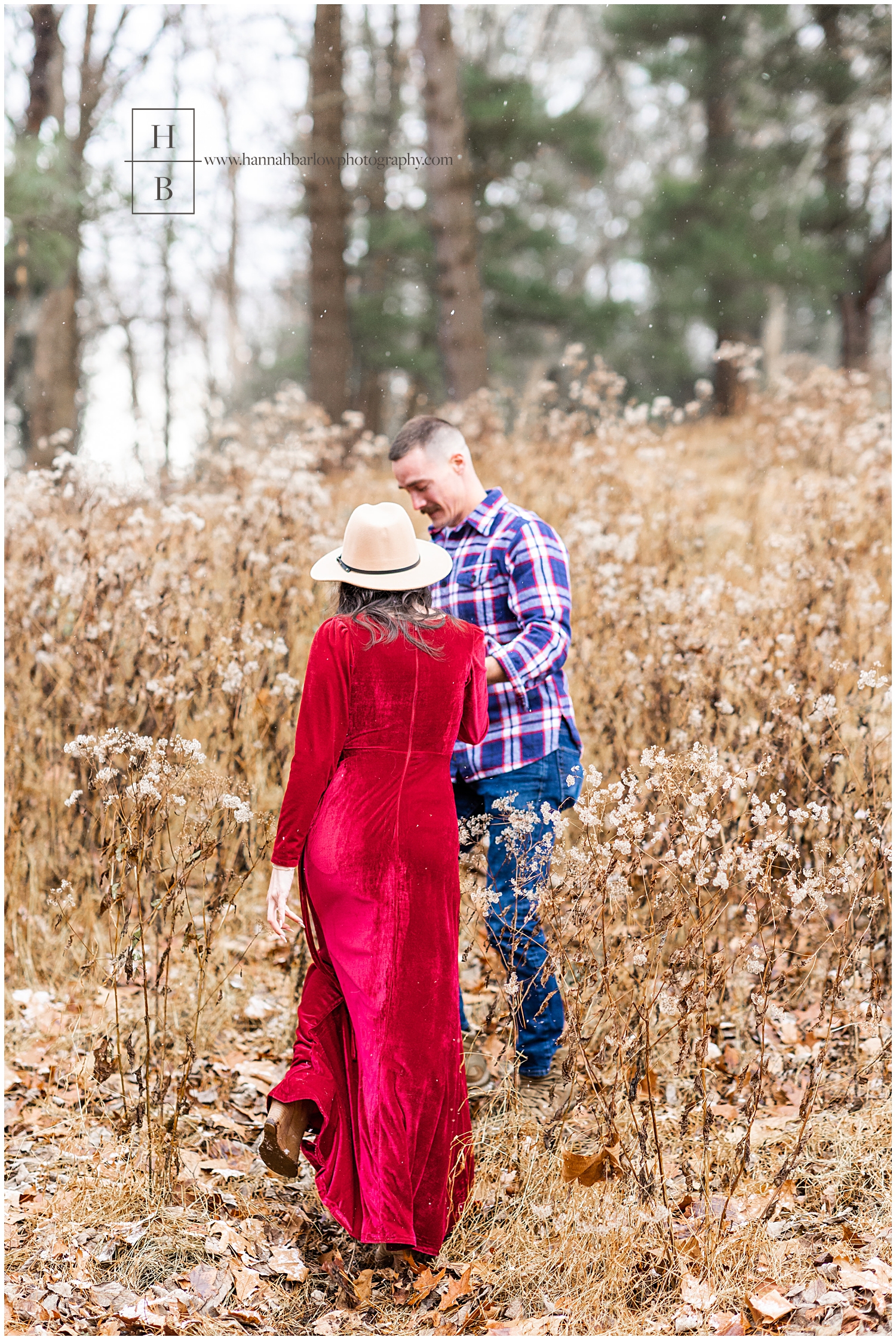 Man in blue flannel shirt escorts wife in red dress into weed line for engagement photos.