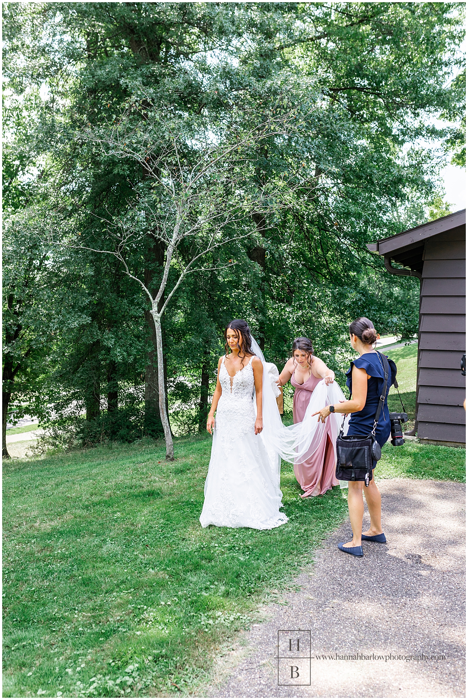 Wedding photographer stands by as bridesmaid arranges bride's train