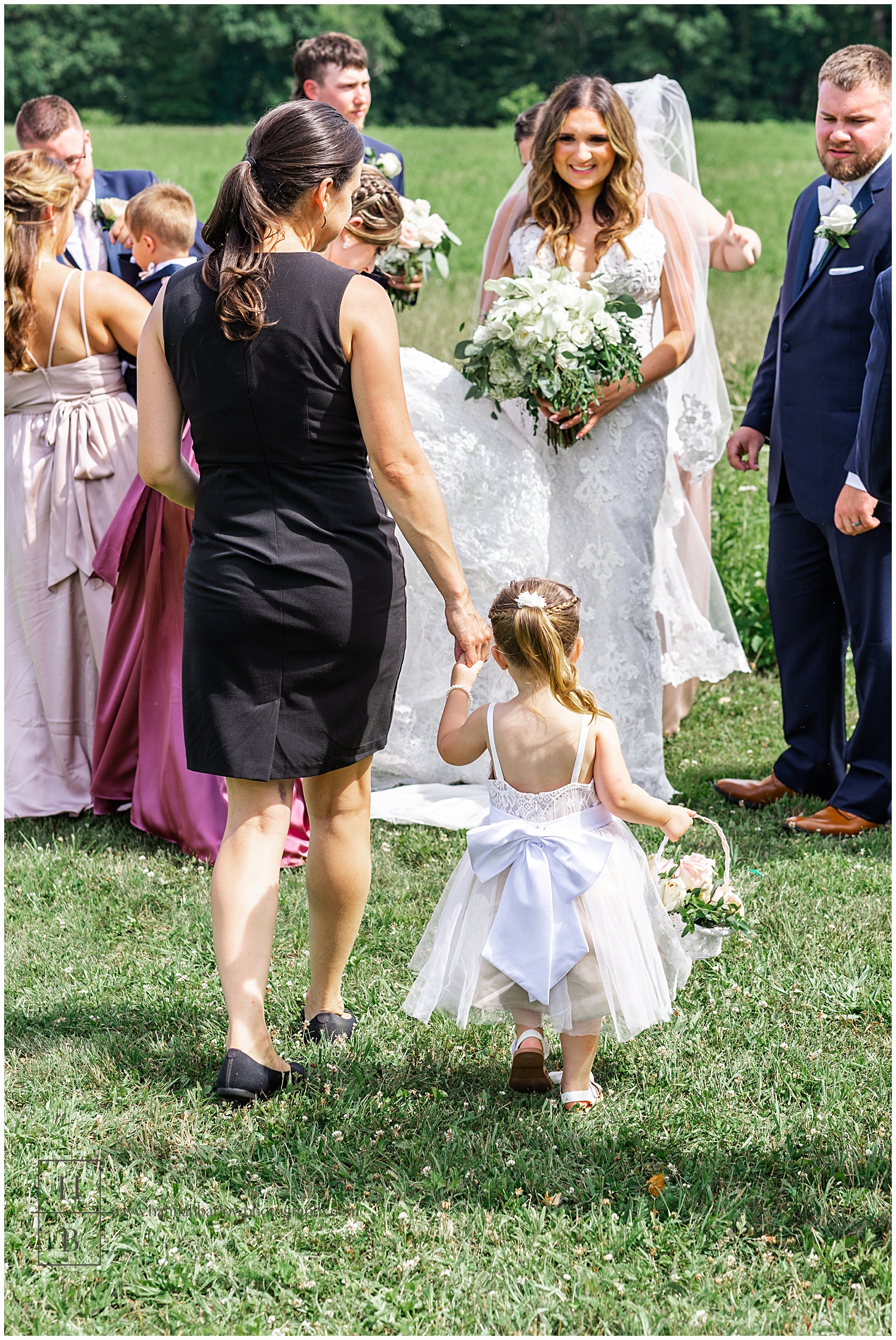 Wedding photographer holds flower girls' hand walking toward bridal party