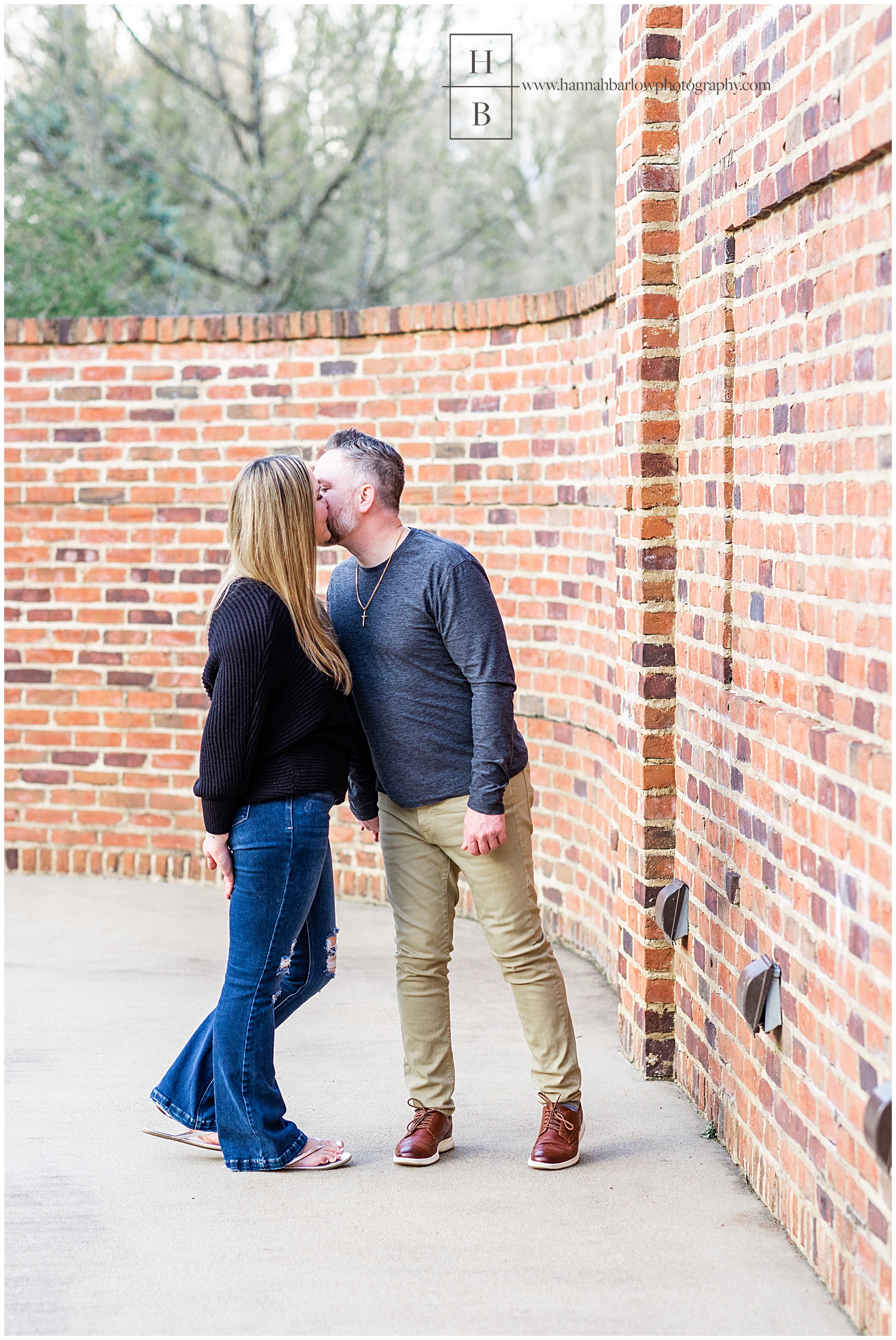 Couple stops walking to kiss by brick wall.