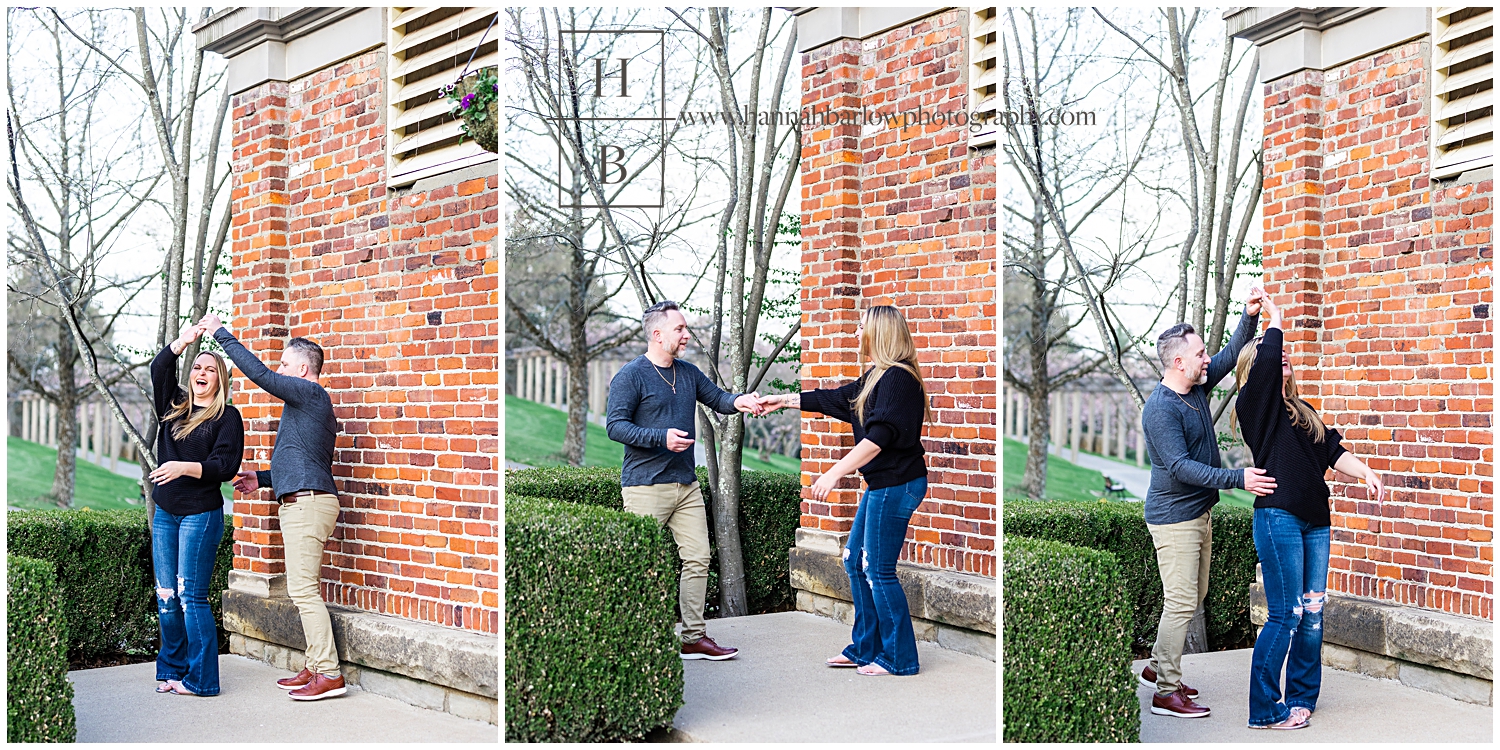 Couple dances for engagement photos by brick wall.