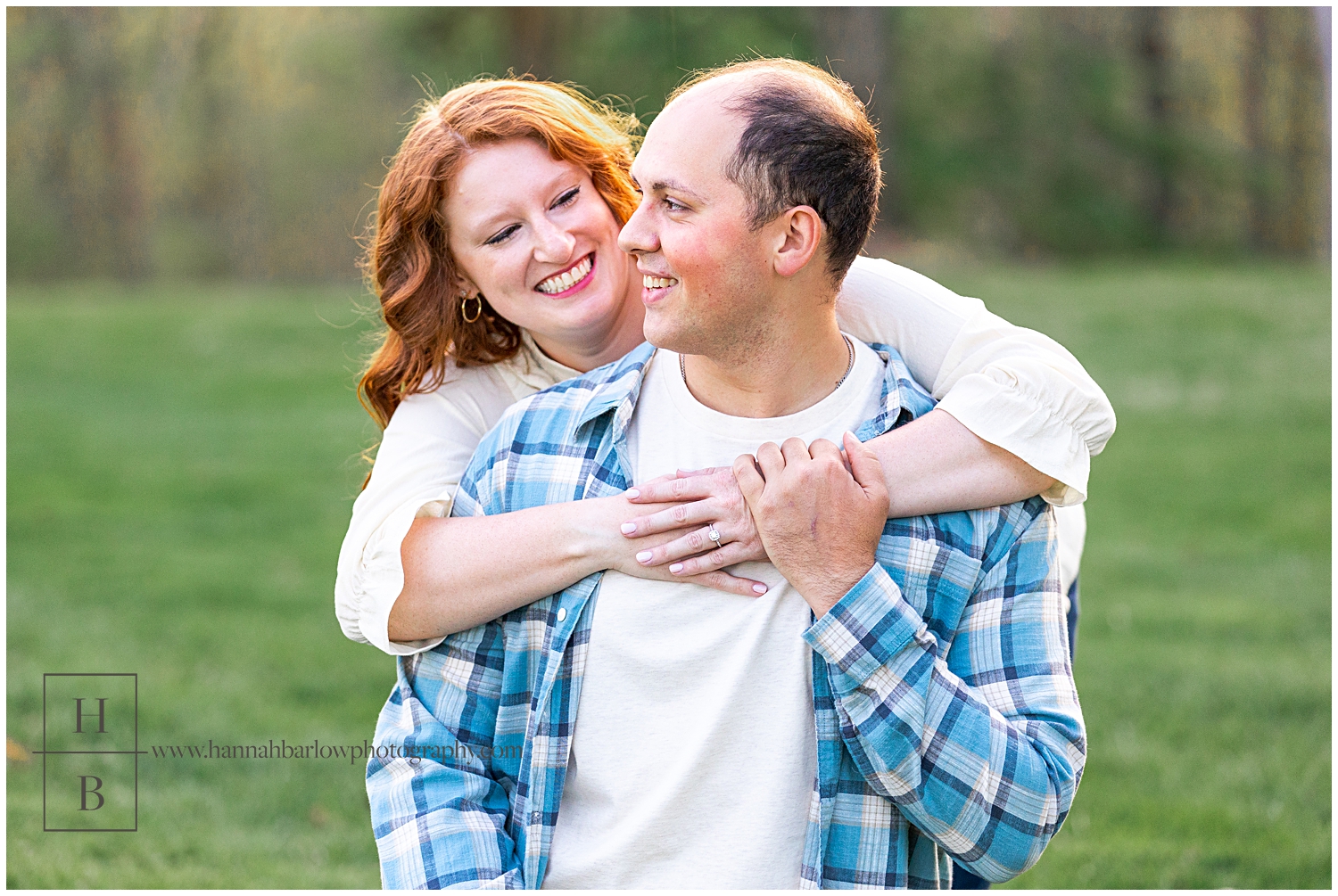 Woman in white blouse hugs fiance in blue flannel from behind.