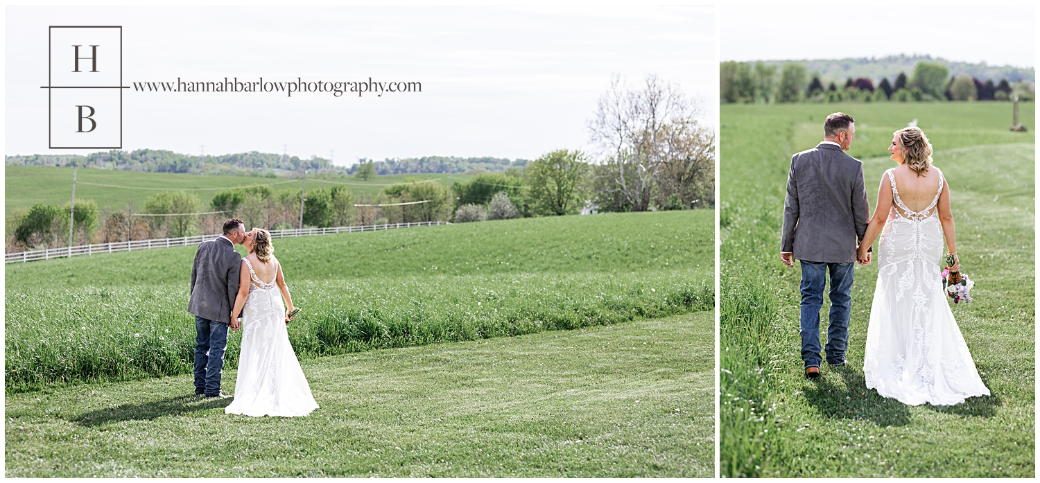 Bride and groom hold hands while walking and stopping for a kiss in field.