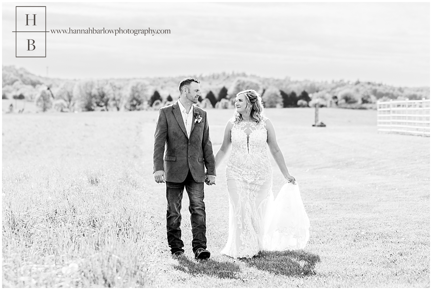 Black and white photo of bride and groom holding hands walking in field.