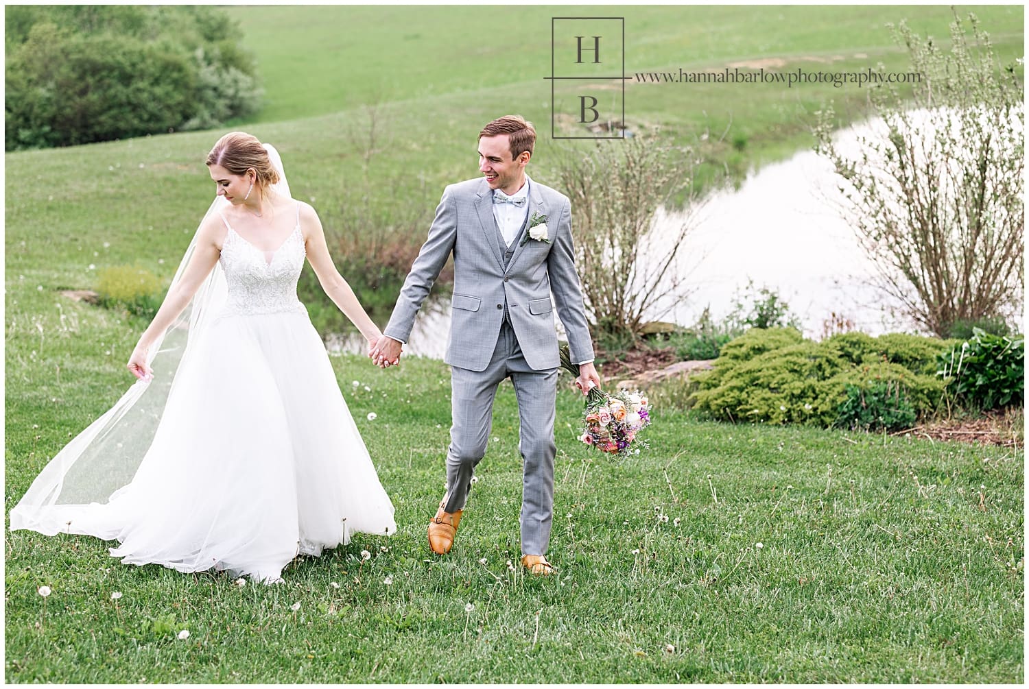 Bride and groom walk hand in hand by lake