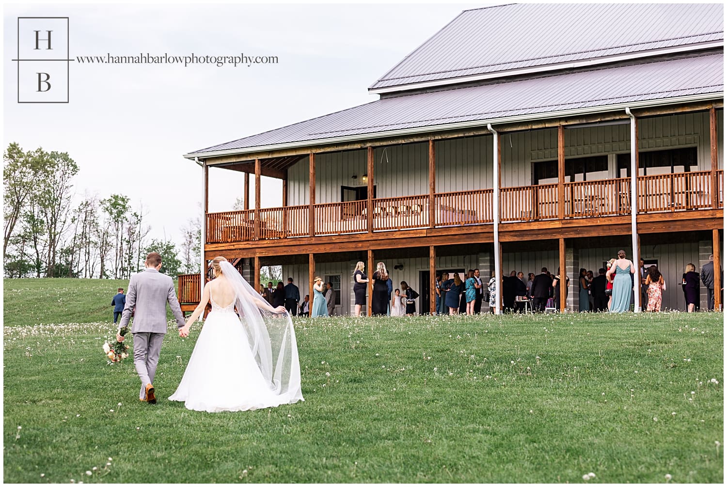 bride and groom walk hand in hand toward cocktail hour at white barn