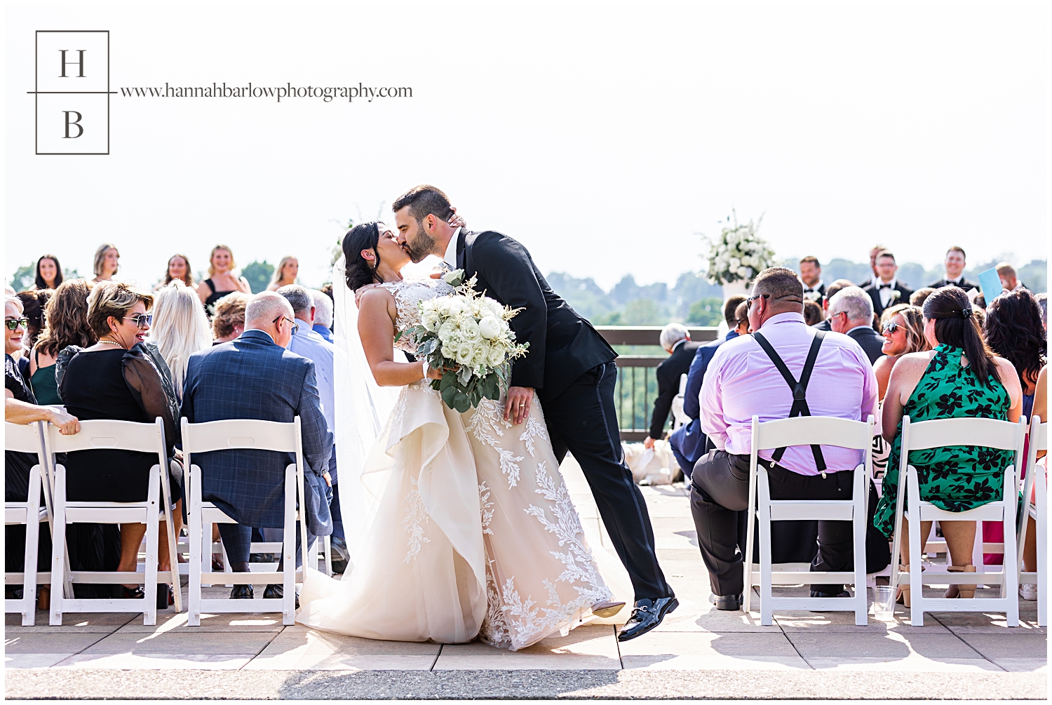 Couple dips for kiss at end of aisle at outdoor patio ceremony.