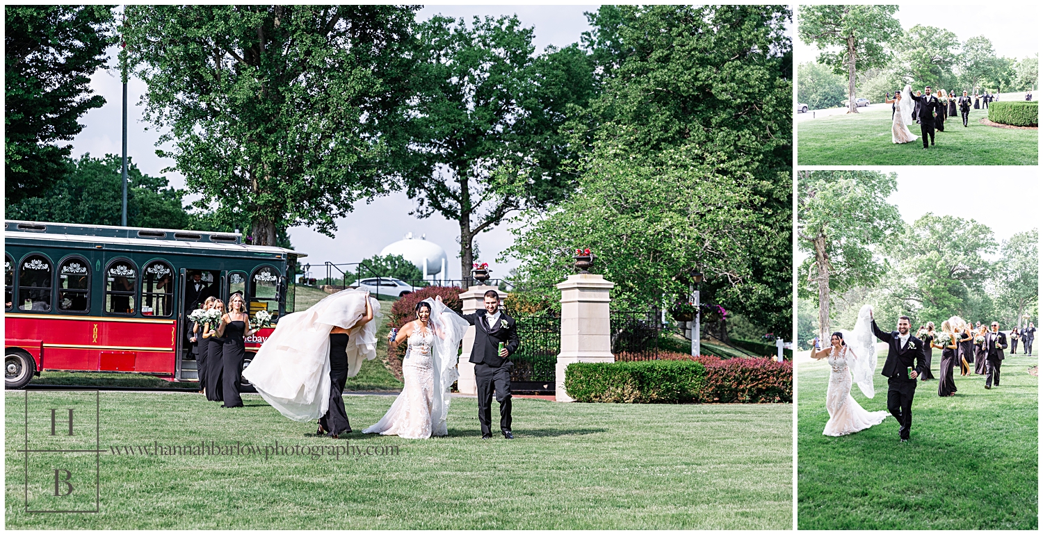 Maid of honor carries brides dress skirt walking away from trolley in green grass.
