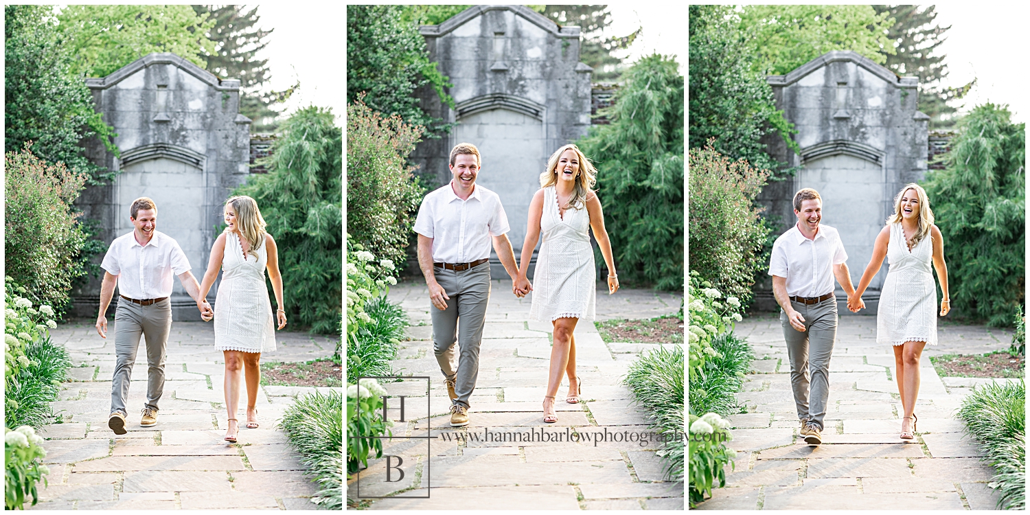 Couple smiles and laughs while holding hands and walking for engagement photos.