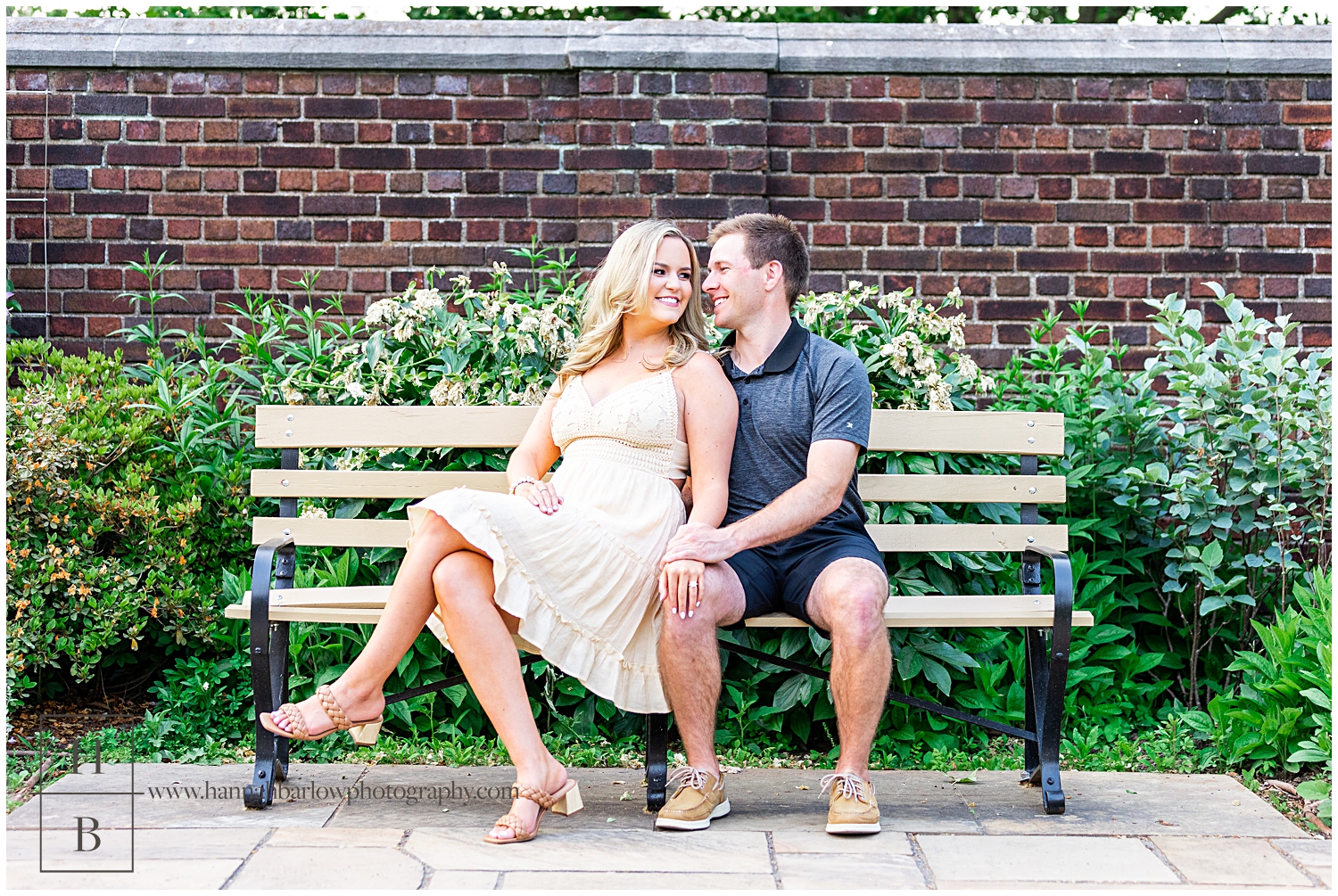 Man and woman sit on bench and pose for engagement photos.