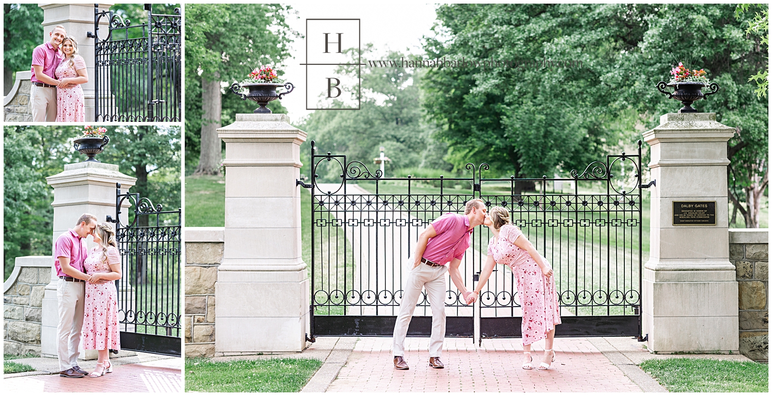 Man and woman in pink embrace by stone Pilars and black iron gates for engagement photos.