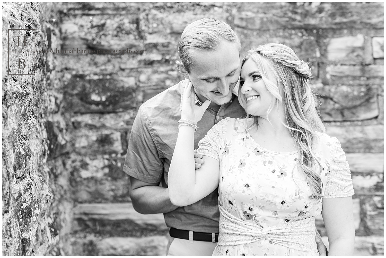 Man stands behind fiancé and embraces her in black and white engagement photo.