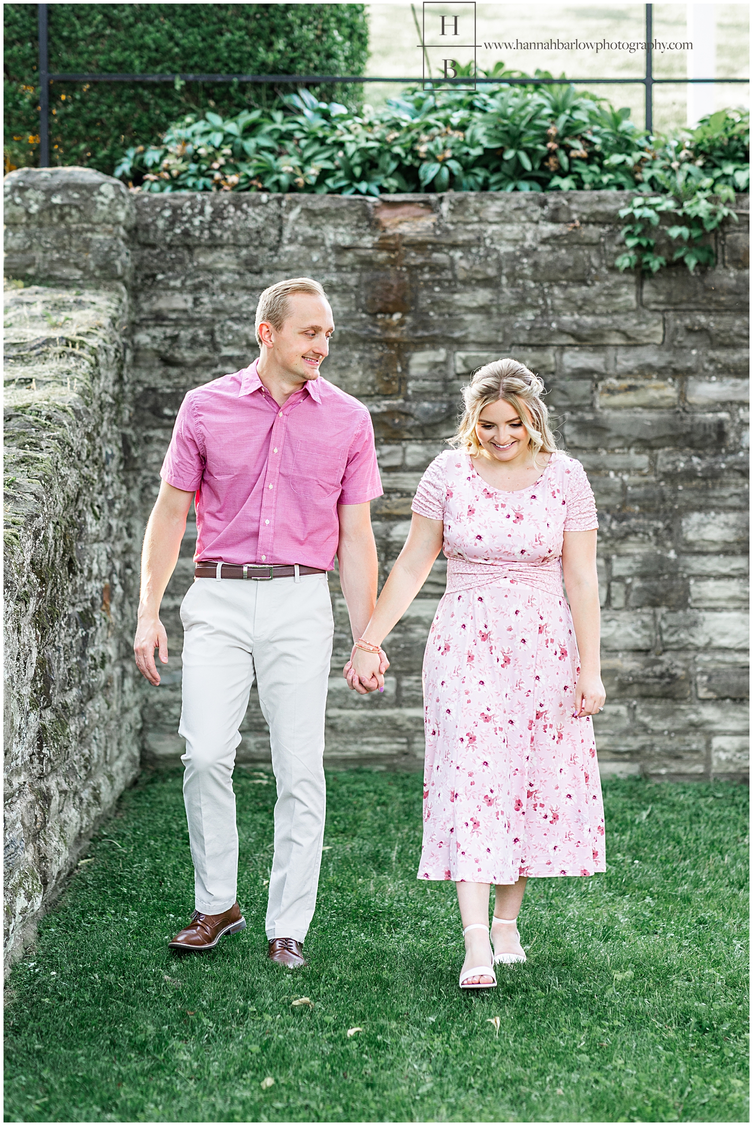 Lady in pink dress walks with fiancé holding hands for engagement photos.
