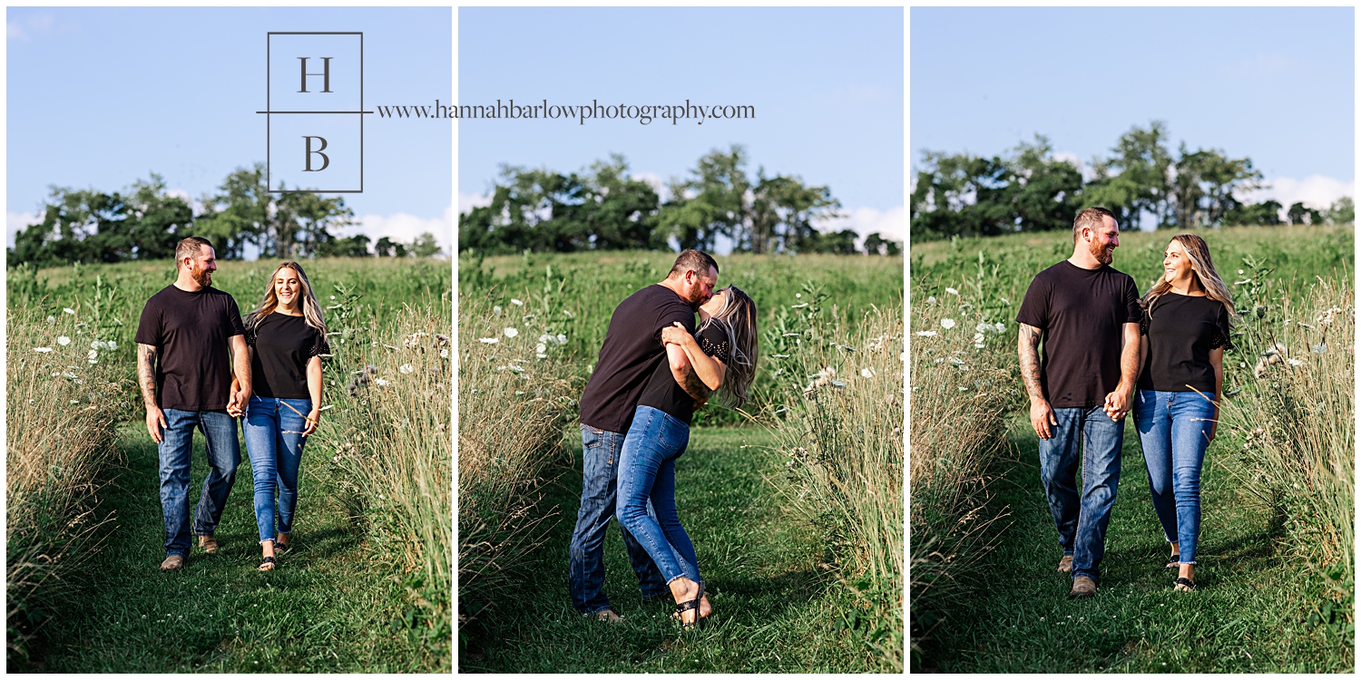 Couple walks down path in field for engagement photos and stop and kiss.