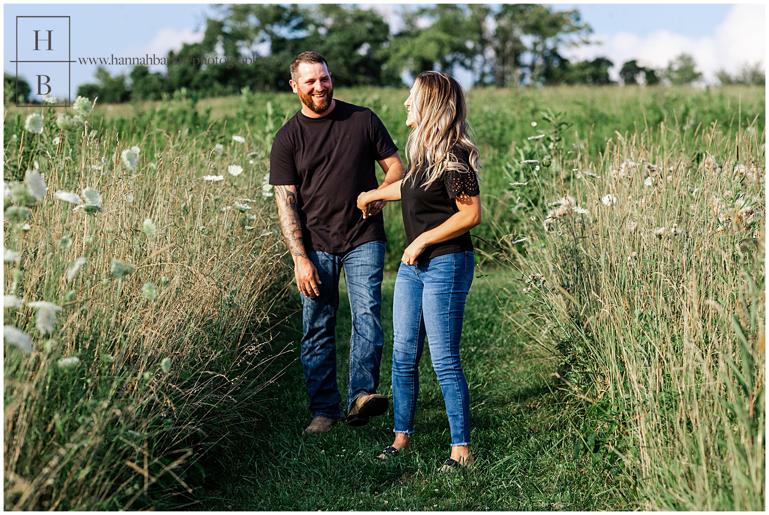 Couple laughs in field wearing black for their engagement photos.