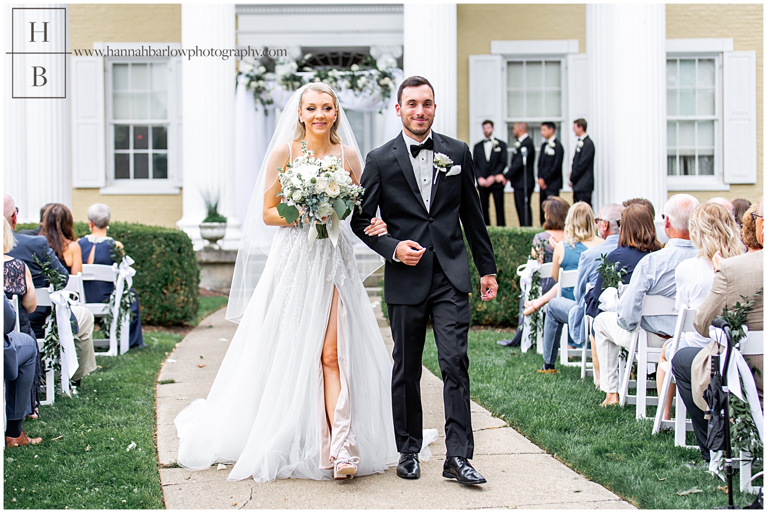 Bride and groom walk down aisle after ceremony in front of yellow Oglebay mansion.