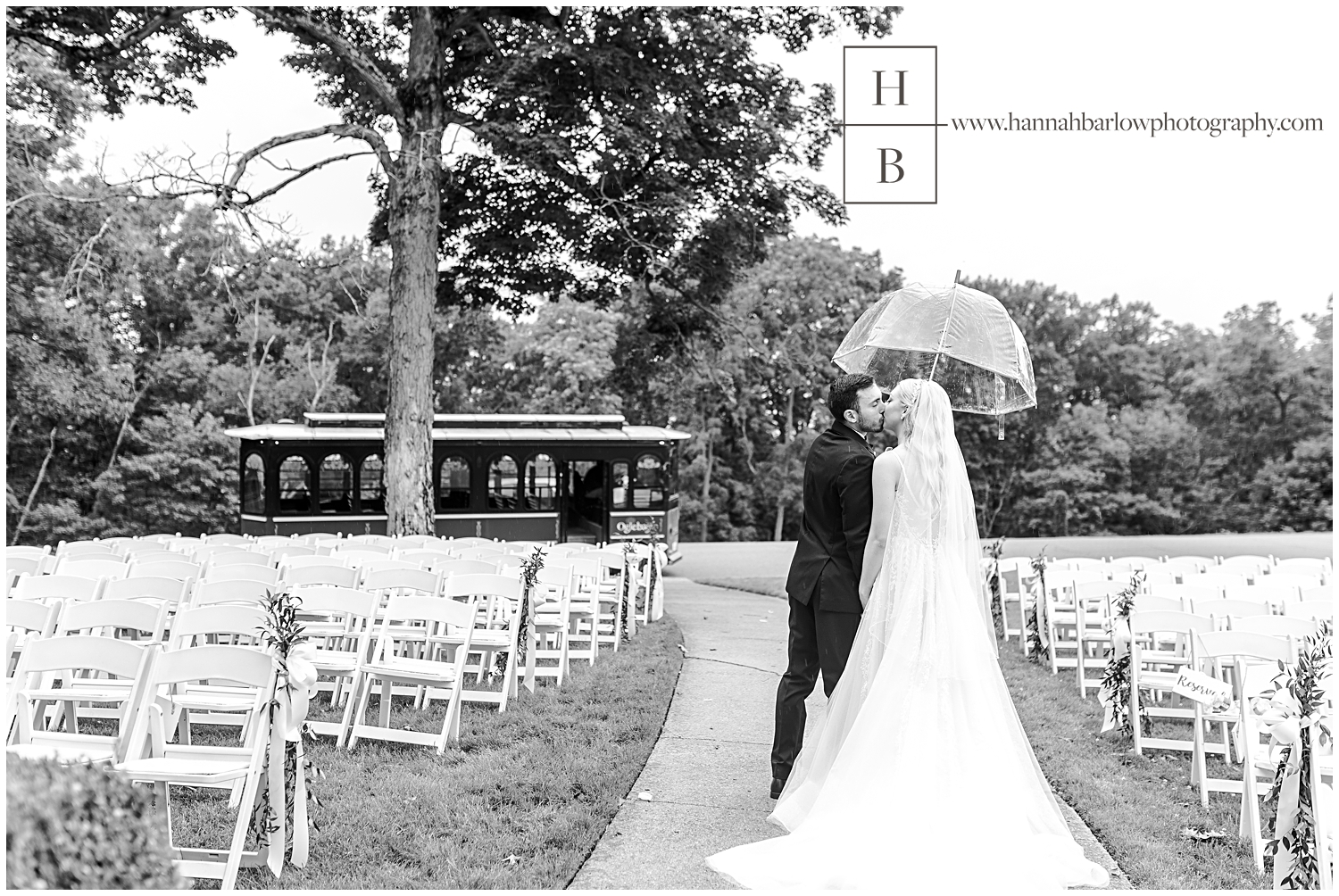 Groom carries umbrella over bride as they walk and kiss.