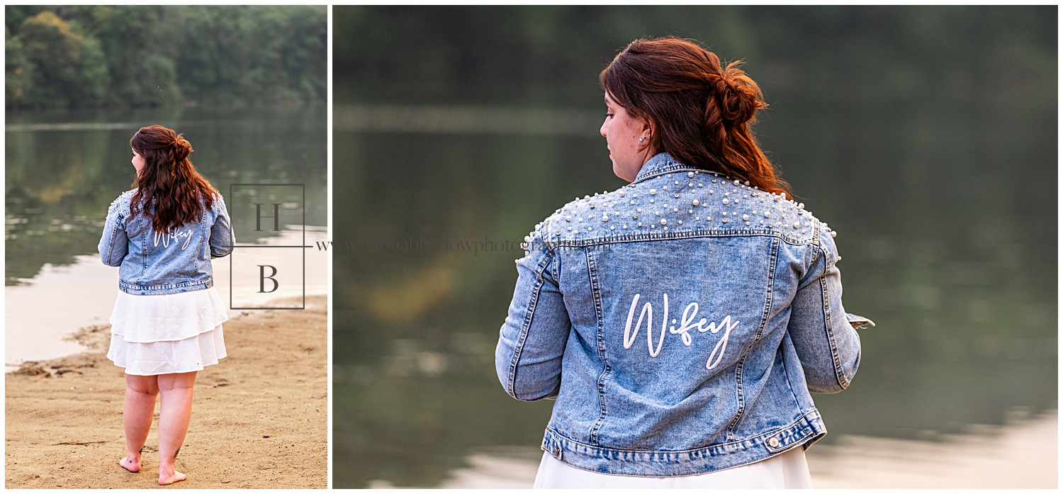 Lady stands by lake in jean jacket that says wifey on the back.