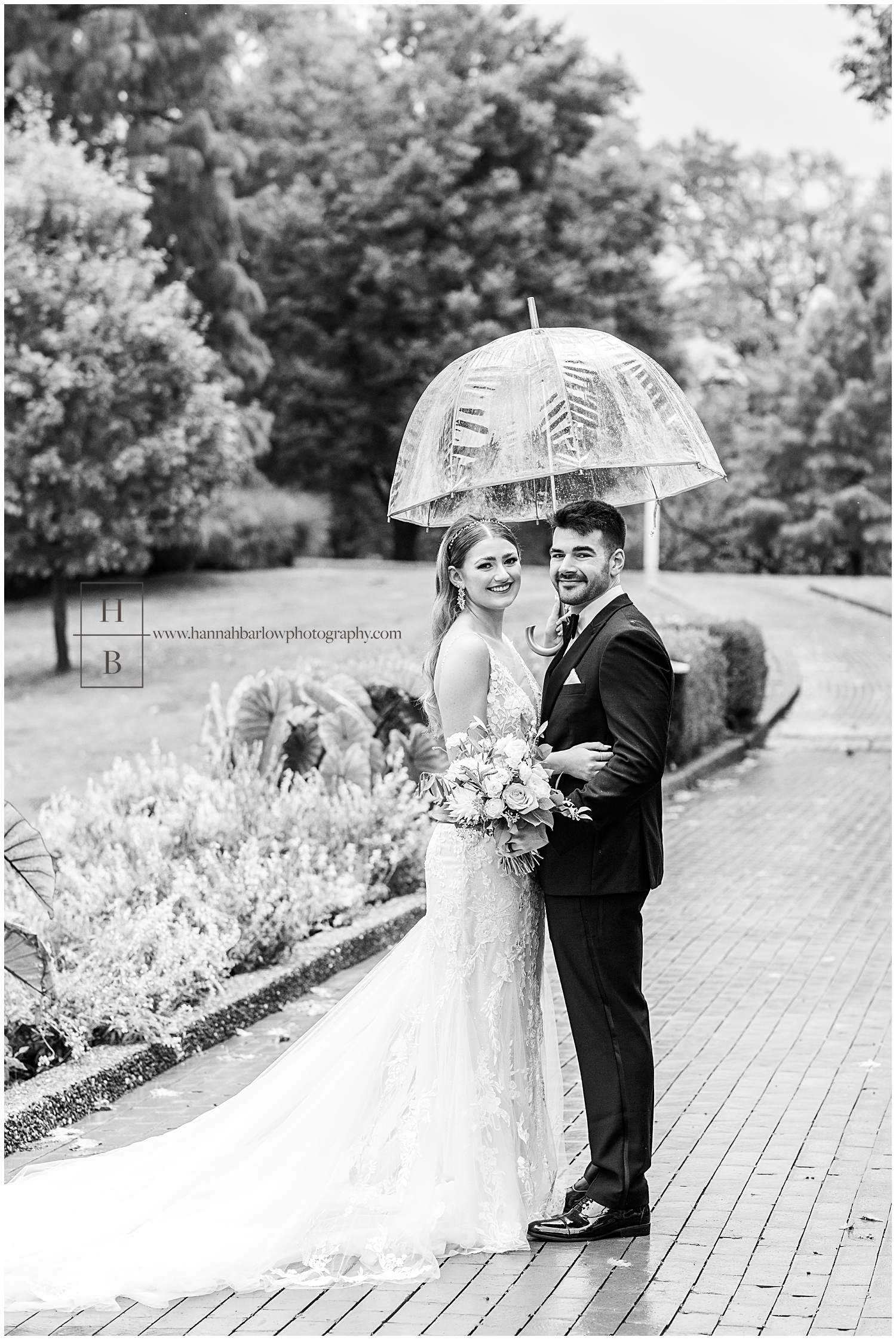 Black and white rainy wedding day photo with bride and groom holding umbrella.
