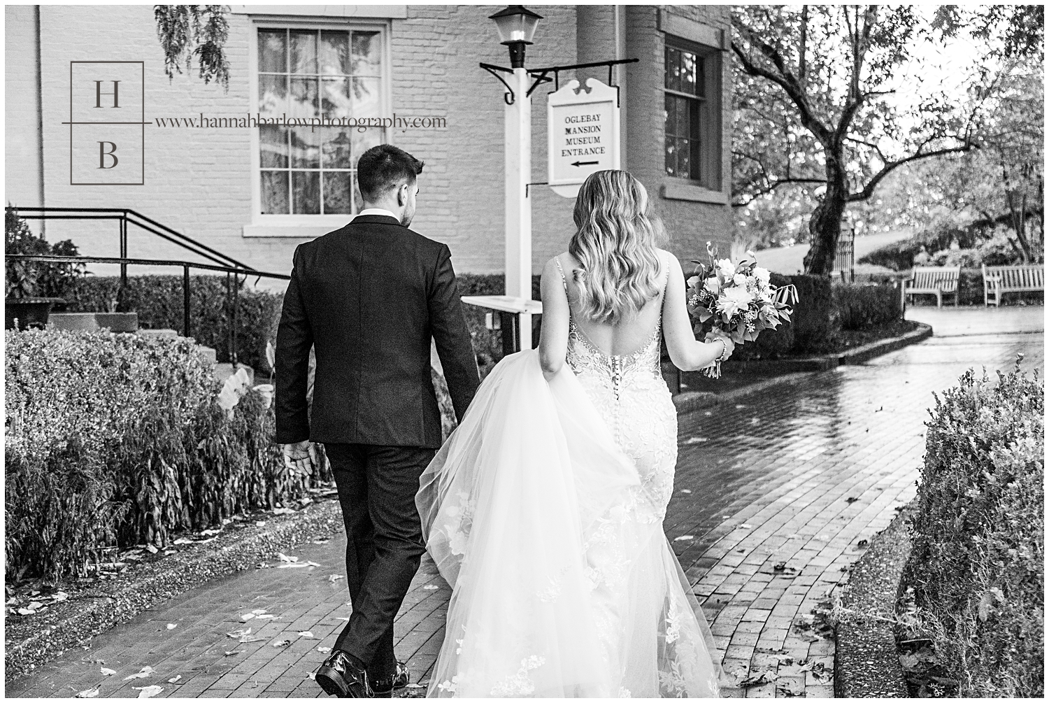 Black and white photo of bride holding dress train up and walking with groom in the rain.