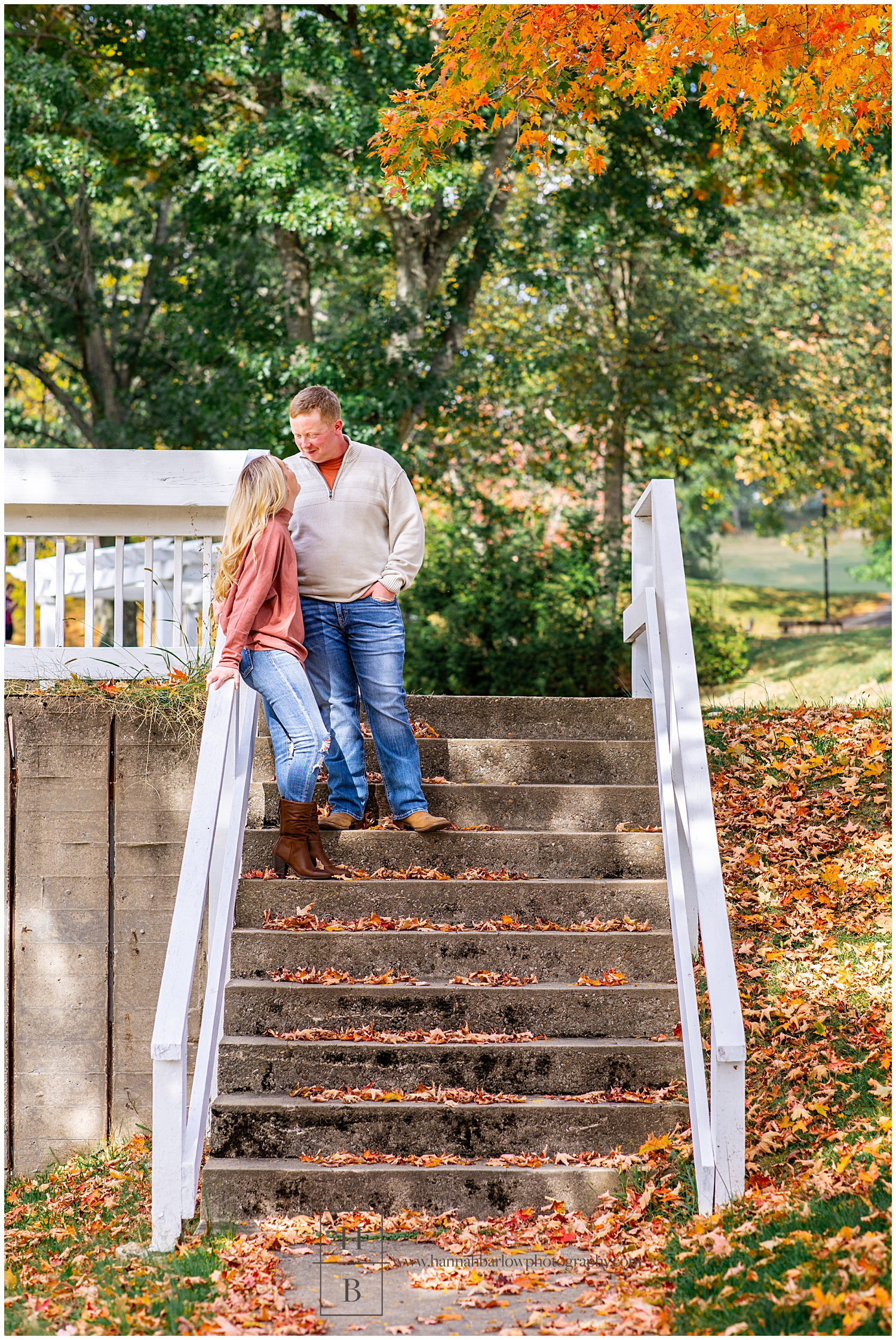 Couple embraces and looks at one another on stone stairs with fall leaves in background.