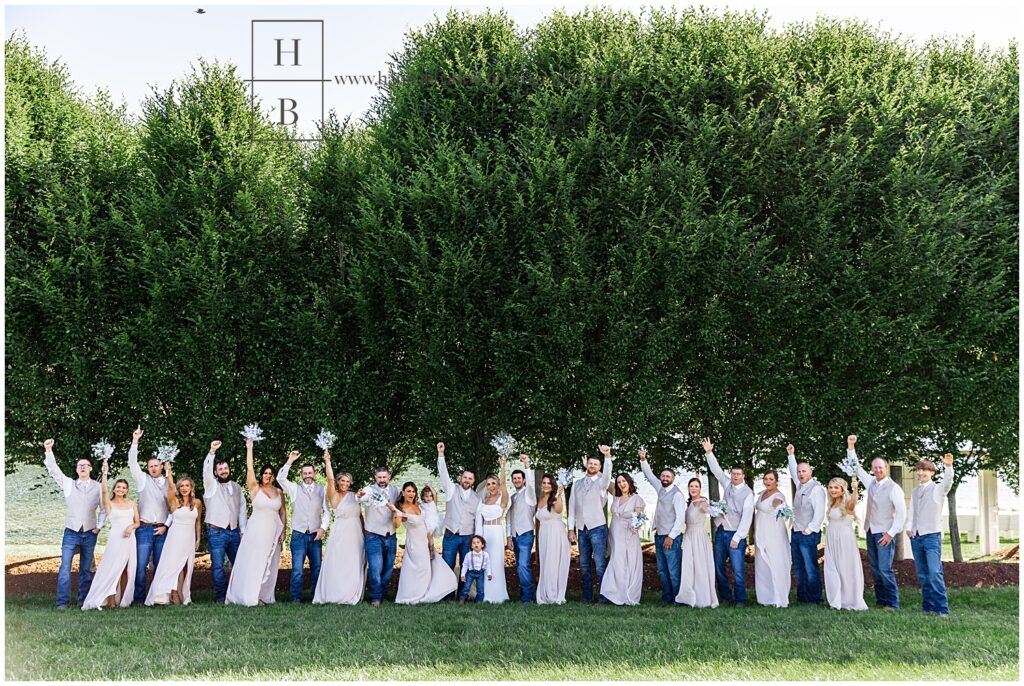 Large bridal party walks in front of trees and cheers