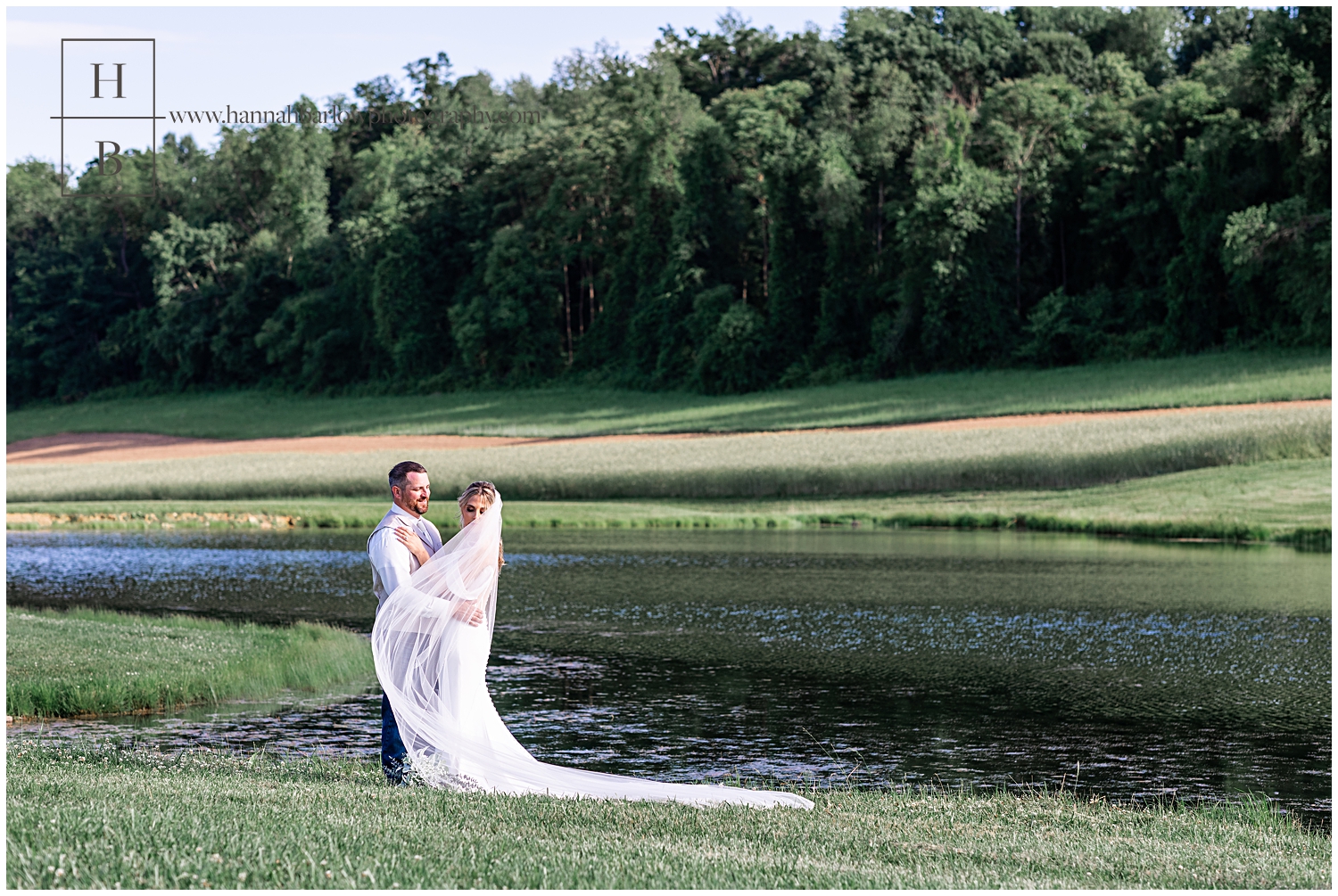 Bride and groom stand by lake and veil blows around bride