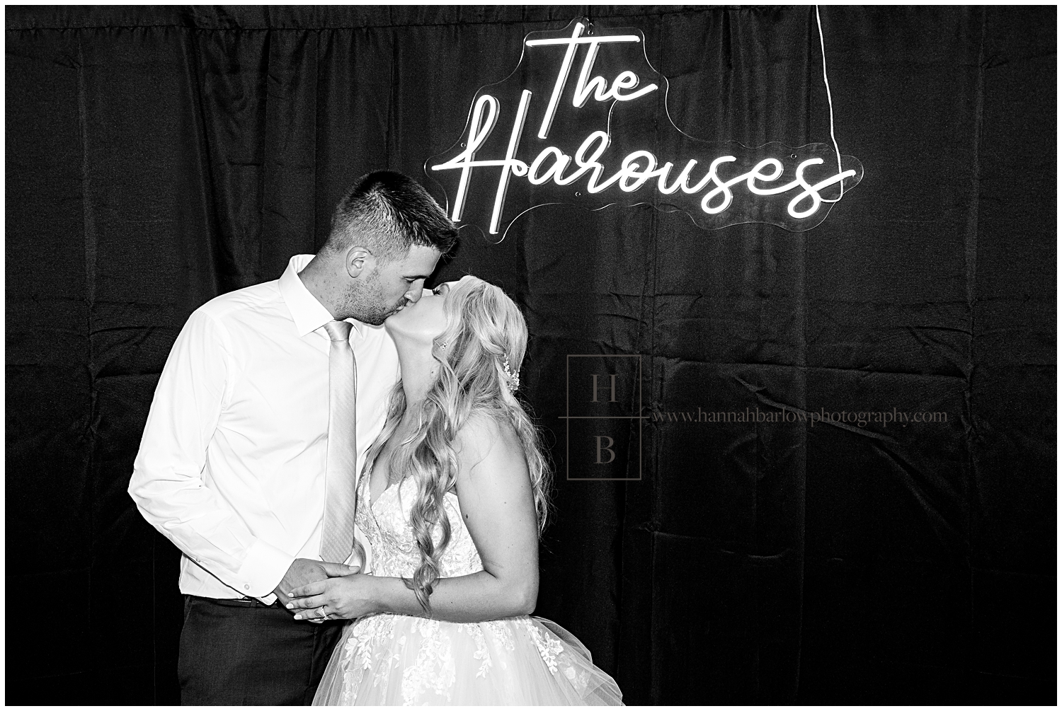 Bride and groom pose by lit up sign with their last name