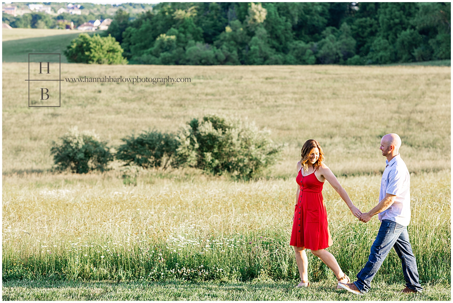 Woman in red dress guides fiancé as they walk by flower field