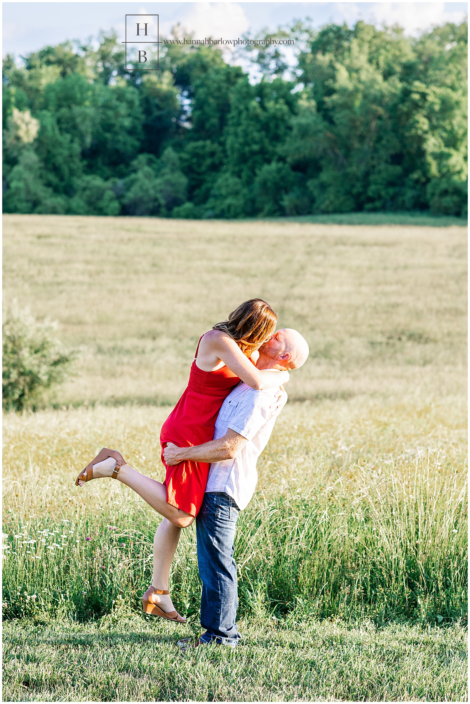 Man holds woman up in the air while they kiss in field