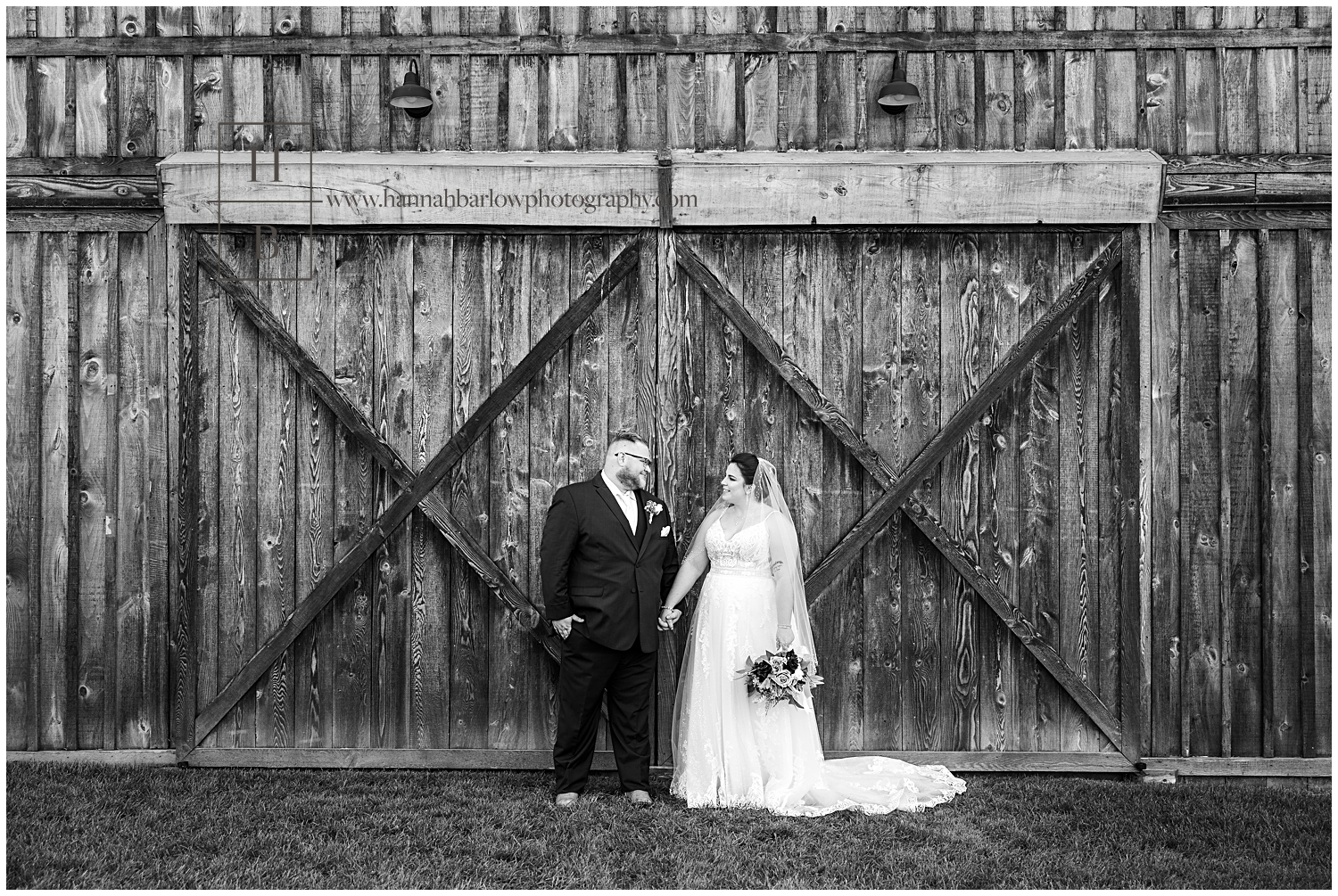 Black and white photo of wedding couple standing next to barn