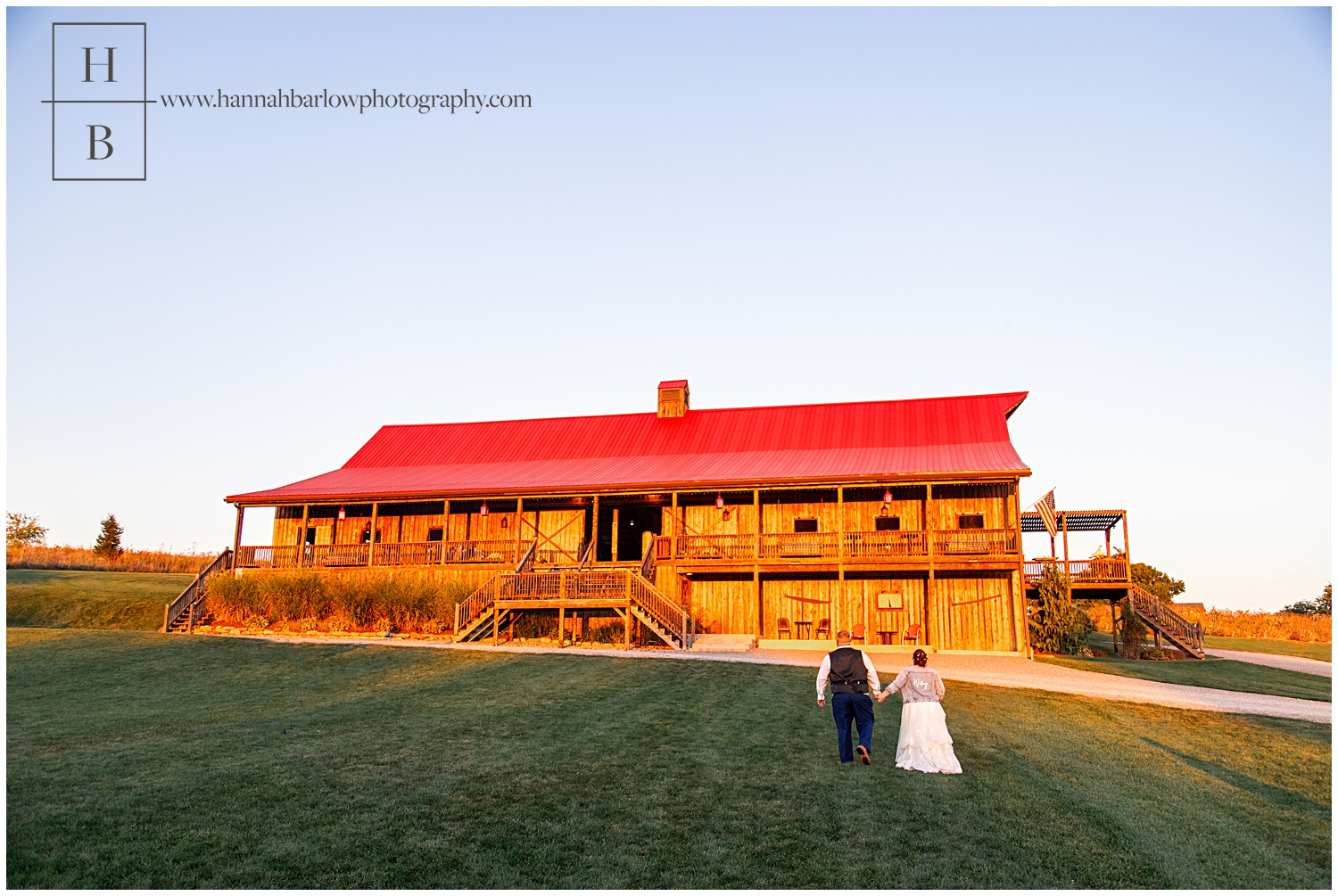 Bride and groom hold hands and walk toward barn