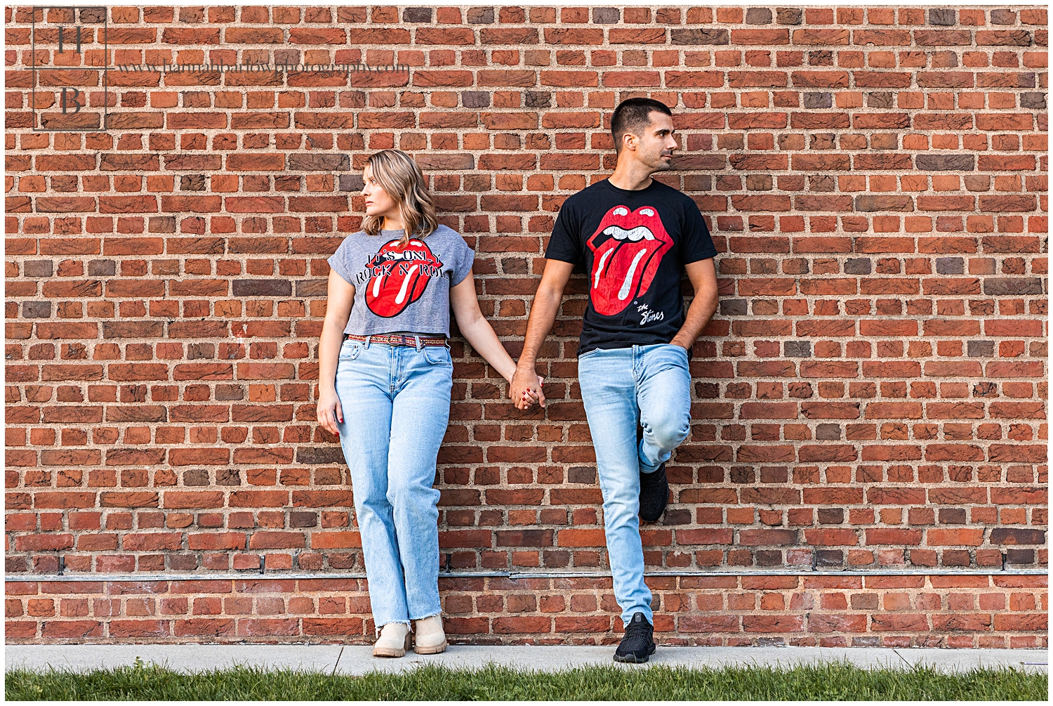 Couple in Rolling Stones shirts hold hands and lean against brick wall