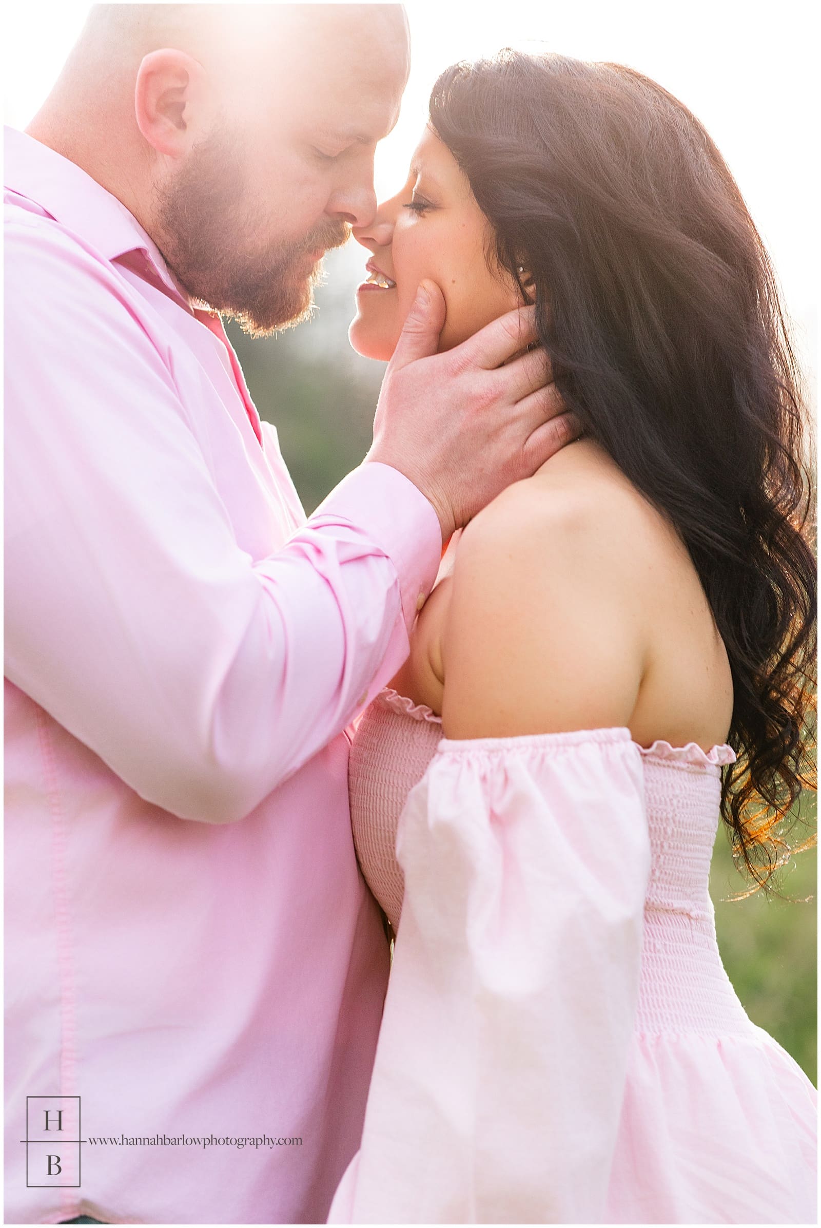 man in pink holds fiancé's head for gentle kiss