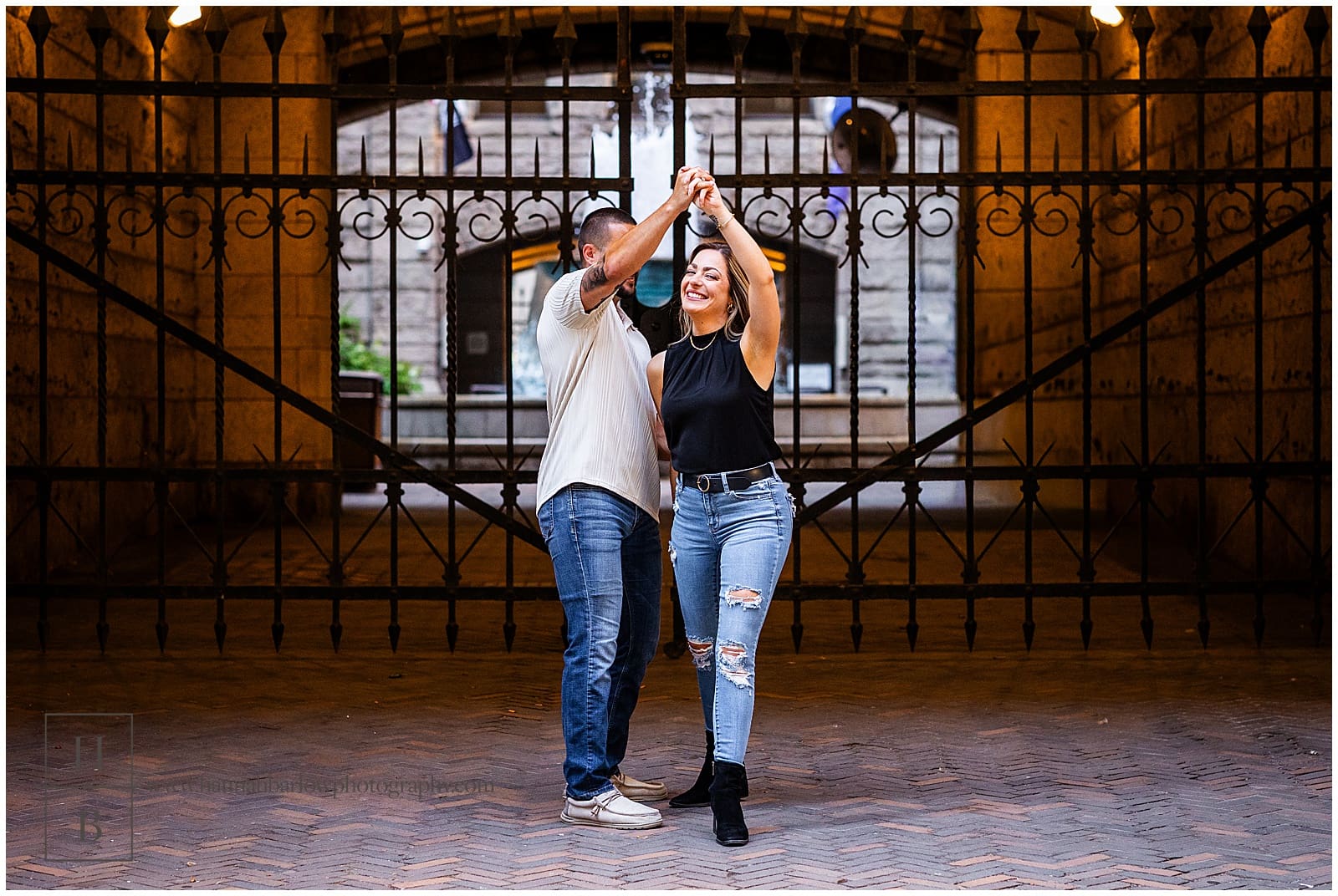 groom to be spins bride for engagement photo in front of iron gates