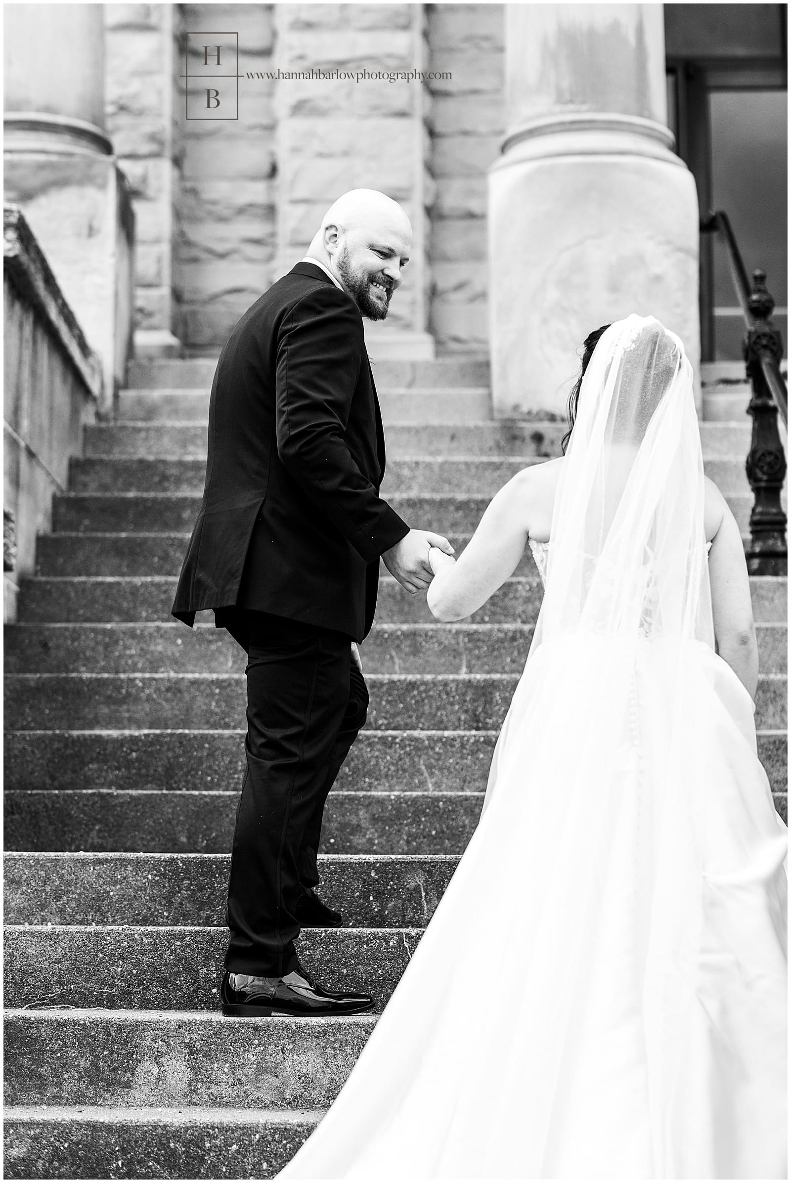 Black and white photo of groom, escorting bride up steps