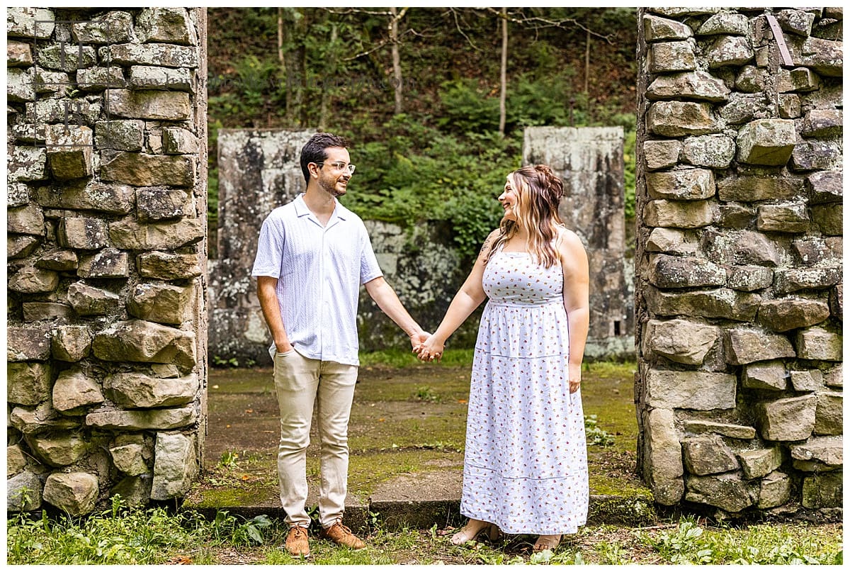 couple poses for engagement photos by old stone building