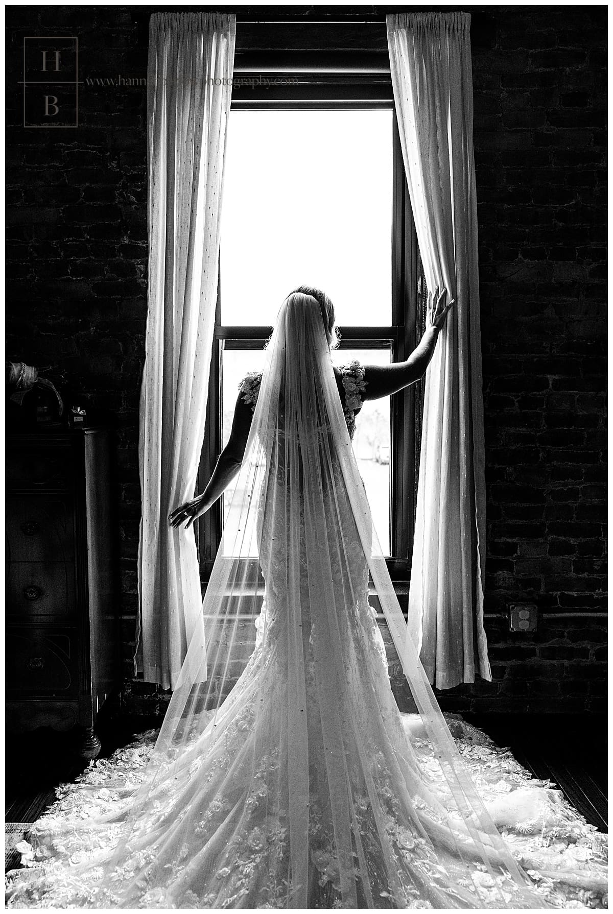 dramatic black and white photo of bride looking out window holding curtains open
