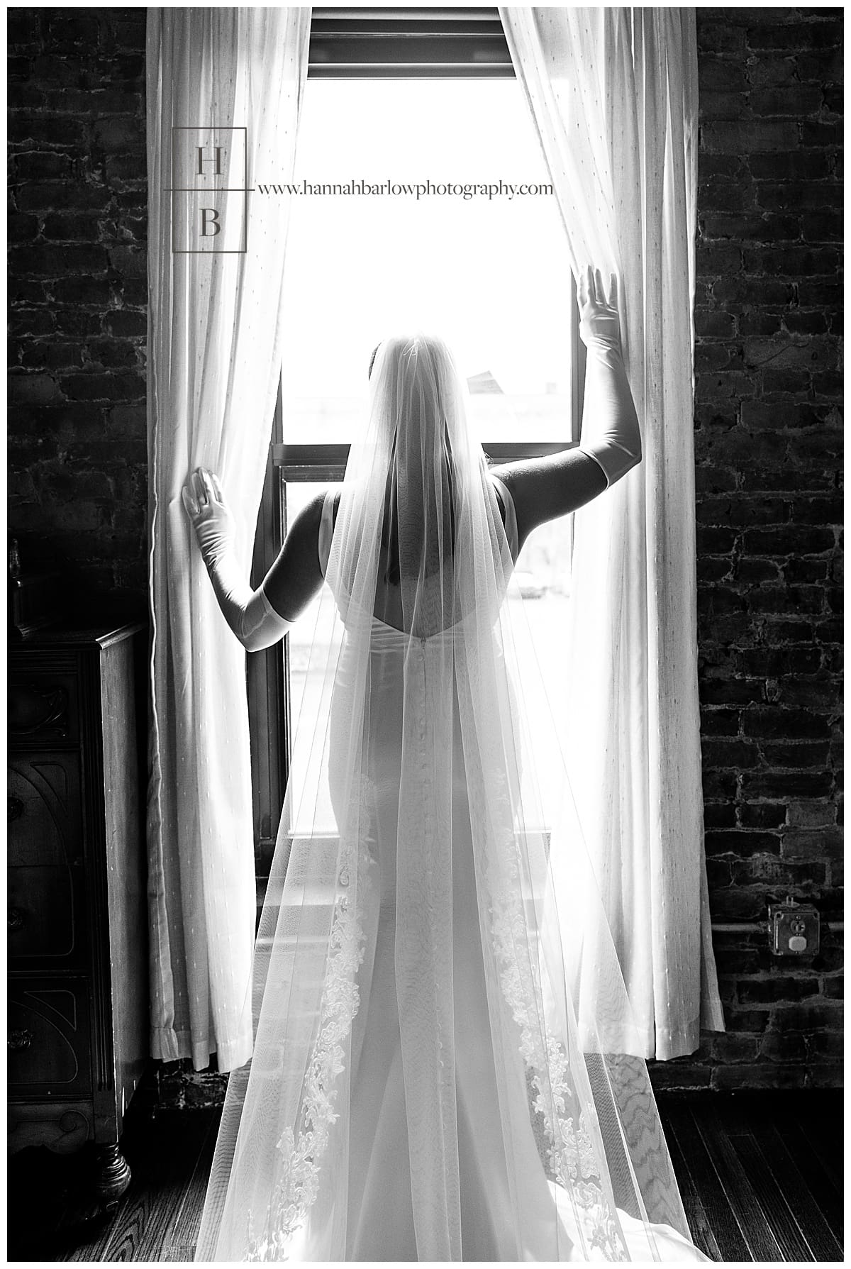 bride dramatically holds curtains open to look out window in black and white photo