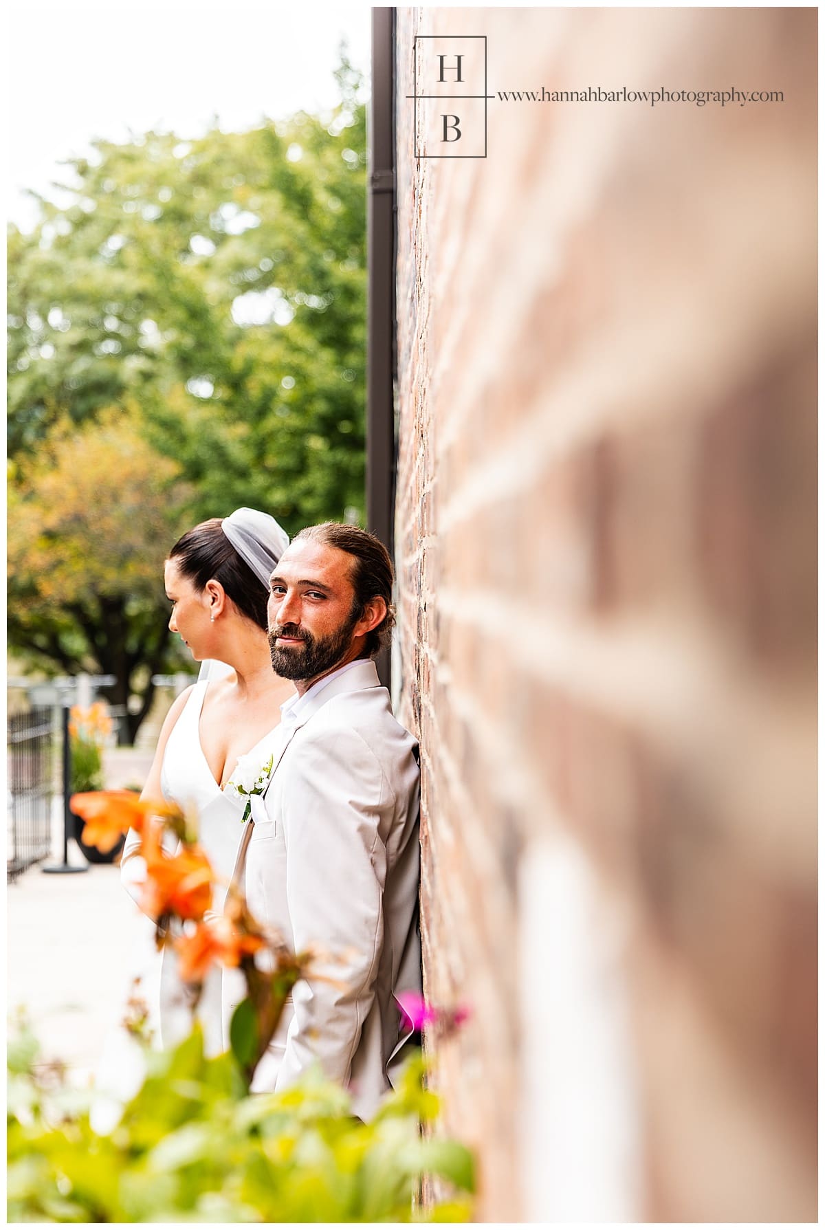 groom leans on brick wall for photo