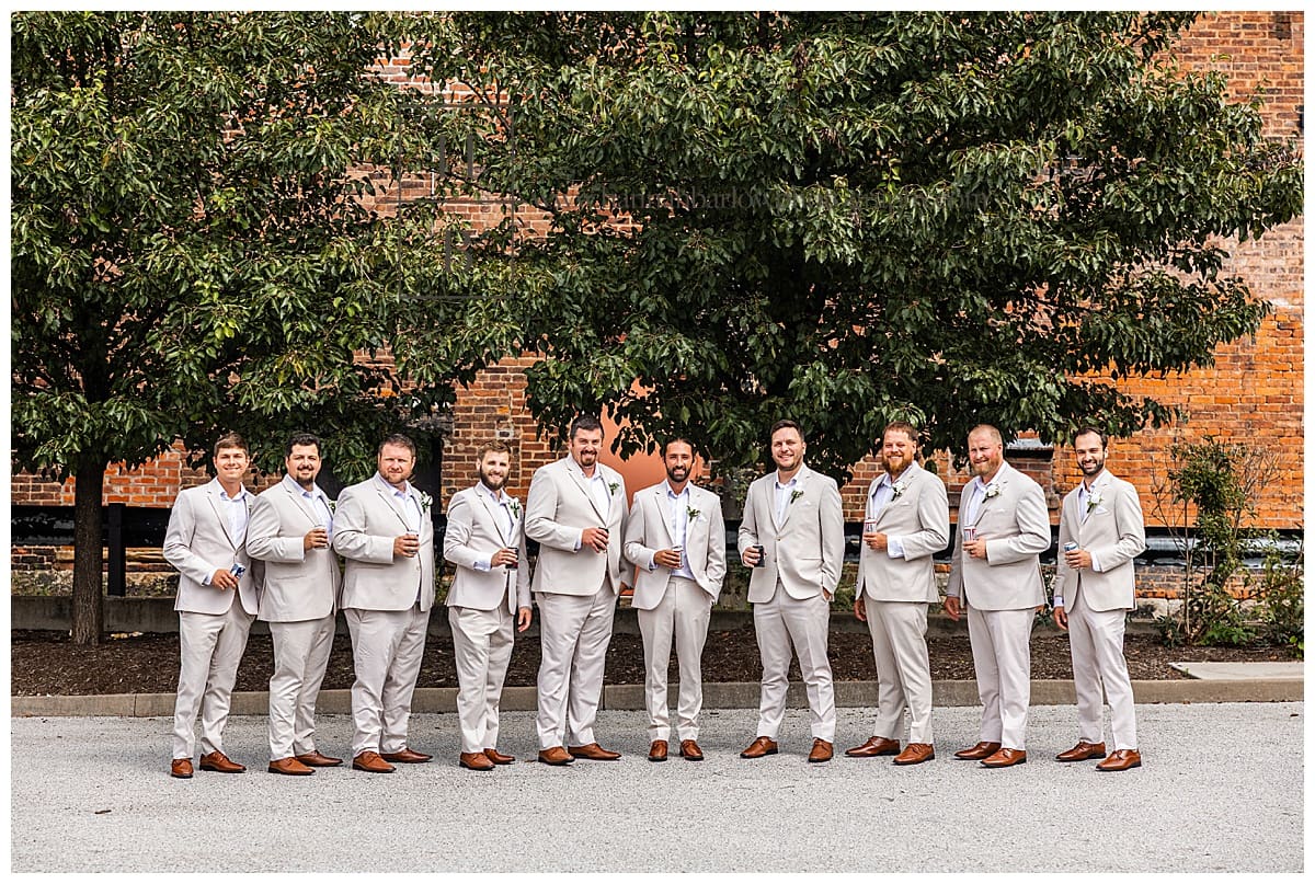groomsmen in tan tuxes pose with beers for wedding photos