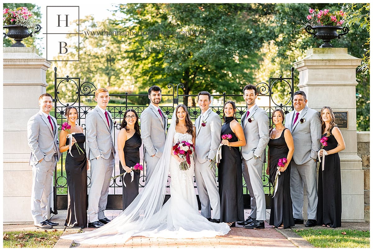 bridesmaids in black dresses and groomsmen in grey tuxes pose with bride and groom